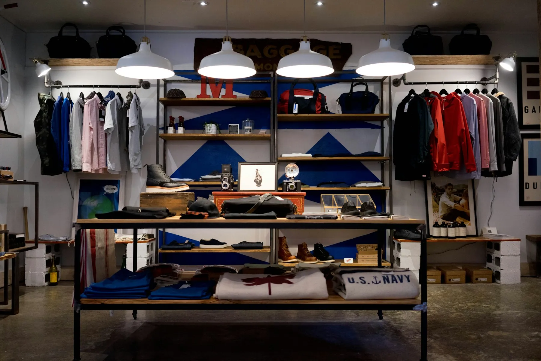 Interior de una tienda de moda con exhibición en mesa central, rieles laterales y lámparas colgantes
